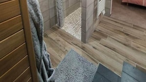 A modern bathroom with a shower, tiled walls, and a wooden floor.
