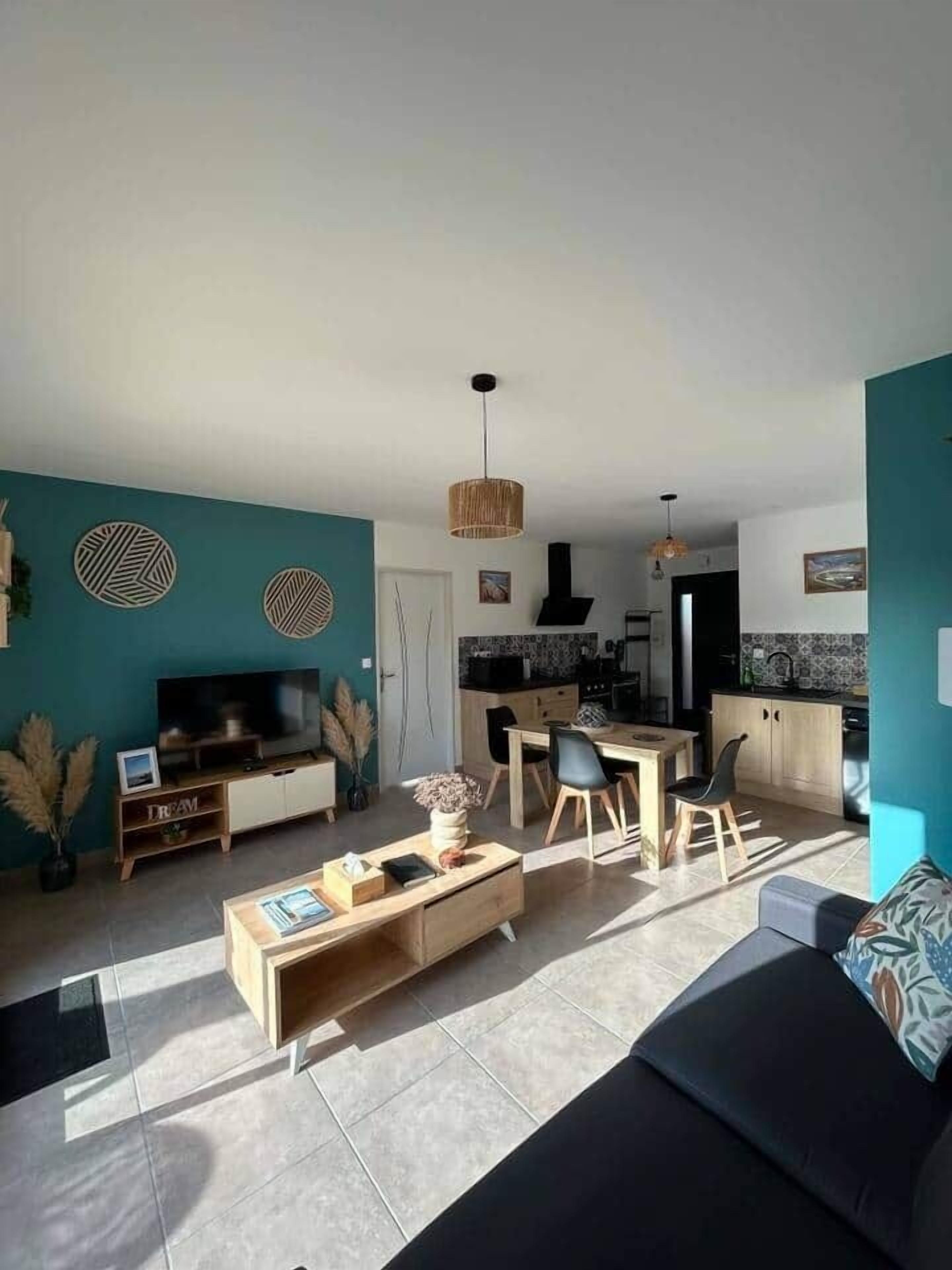 A modern living room with a sofa, coffee table, and TV, a dining area with chairs, and a kitchen with a stove and cabinets.