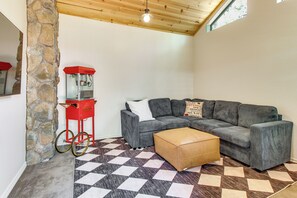 A cozy living room with a checkered floor, a grey sectional sofa, a red popcorn machine, and a stone wall. - Deck, Fire Pit, Hot Tub! Pinetop Family Cabin (Pinetop)