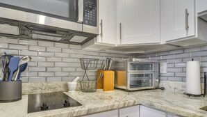 Een keuken met witte kastjes, een roestvrijstalen afzuigkap, een magnetron, een dubbele oven en een marmeren aanrecht.