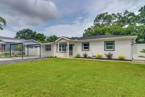 A single-story house with a covered garage, a front yard with grass, and a white fence. - Work & Relax in Safety Harbor! Modern Coastal Apt (Safety Harbor)