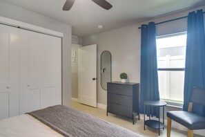 Une chambre à coucher avec un lit, une commode, une chaise, un miroir et une fenêtre avec des rideaux.