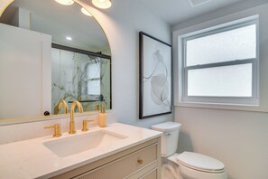 Une salle de bain avec un lavabo blanc, des robinets dorés, des toilettes et une œuvre d’art encadrée accrochée au mur.