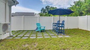 Een achtertuin met een wit hek, een blauwe Adirondack-stoel, een bijpassende tafel en een blauwe parasol.