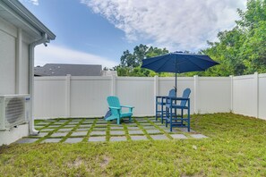 A backyard with a white fence, a blue Adirondack chair, a matching table, and a blue umbrella. - Work & Relax in Safety Harbor! Modern Coastal Apt (Safety Harbor)