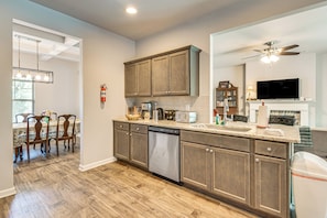 A modern kitchen with wooden cabinets, a dishwasher, and a dining area with chairs and a table. - Near Parks, Dining & Shopping! Newnan Family Home (Newnan)