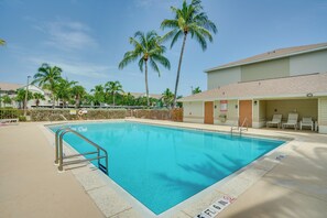 Una piscina con una scala metallica, circondata da palme e un edificio con una zona coperta.