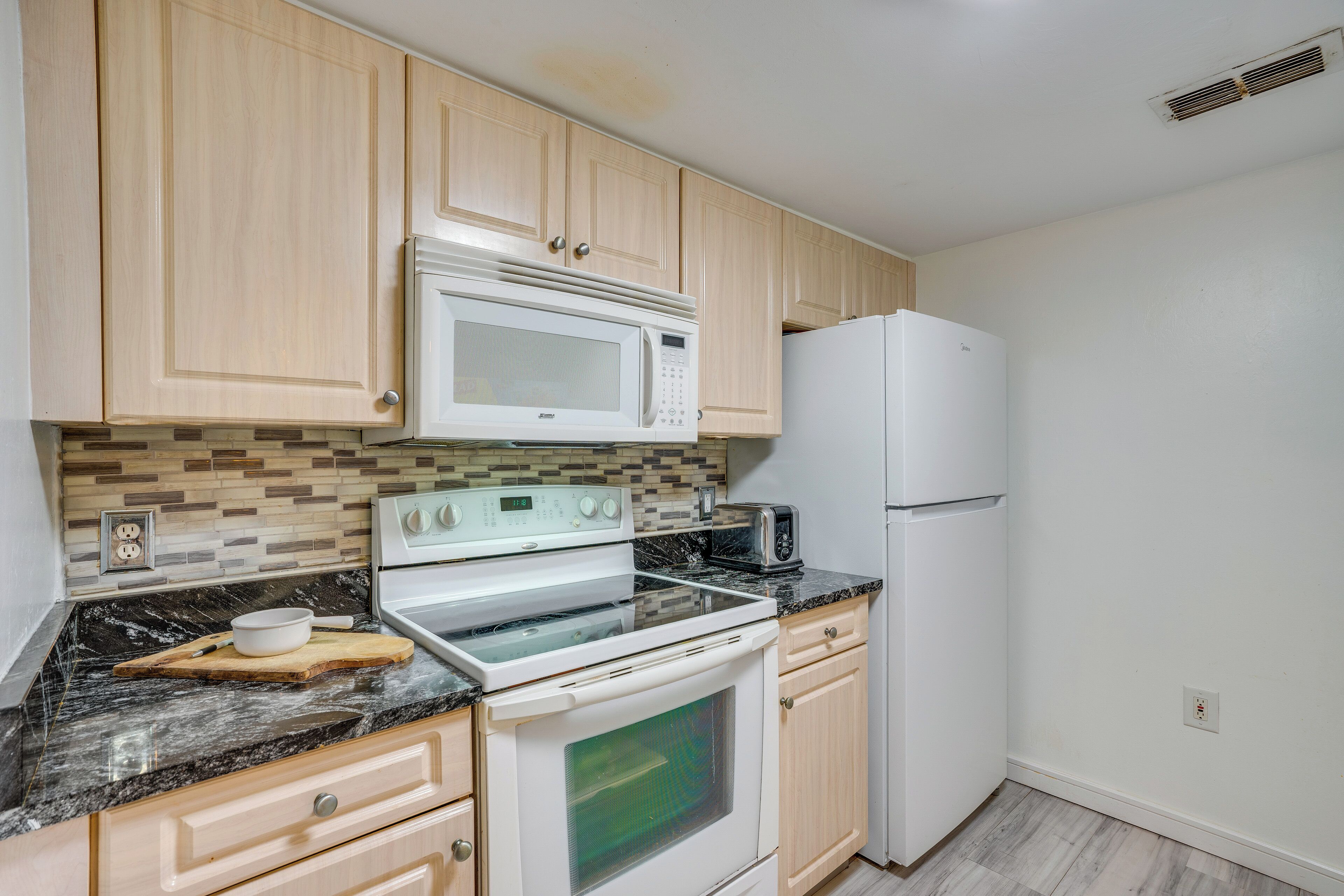 Una cocina con armarios de madera, microondas, estufa, refrigerador y salpicadero de azulejos.