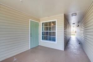 Un pasillo con una puerta verde, un ventanal con persianas y vista a una habitación con ventilador de techo.