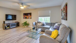 A modern living room with a flat-screen TV, a glass coffee table, a sofa with decorative pillows, and a ceiling fan. - Walk to Shops & Eats! Cape Coral Extended Escape (Cape Coral)