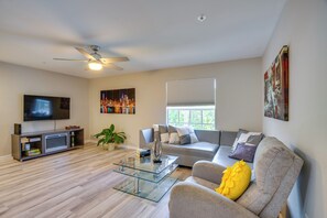 A modern living room with a flat-screen TV, a glass coffee table, a sofa with decorative pillows, and a ceiling fan. - Walk to Shops & Eats! Cape Coral Extended Escape (Cape Coral)