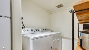 Et kompakt vaskerum med en hvid Whirlpool vaskemaskine og tørretumbler, en træhylde og et lille vindue.