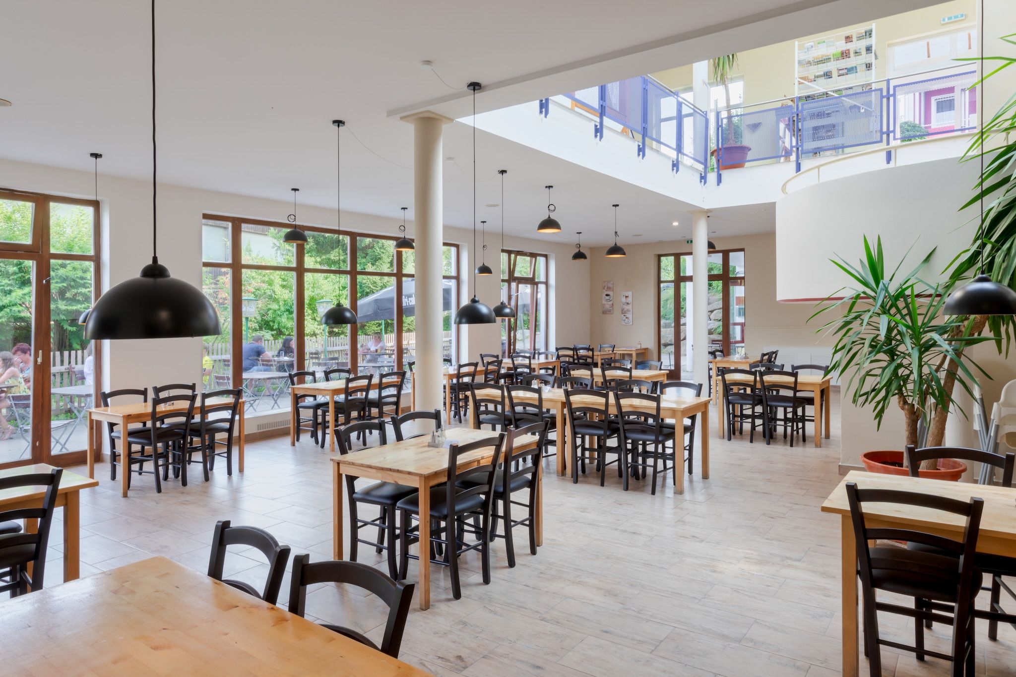 A spacious indoor dining area with multiple tables and chairs, large windows, and hanging pendant lights.