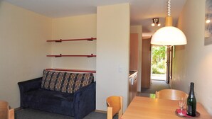 Een knus woongedeelte met een bank, een eettafel met fles en glazen, en een gang naar een andere kamer.