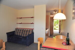 A compact living space with a sofa, a dining table with a bottle and glasses, and a hallway leading to another room. - Appartement mit All inklusive Angebot und Pool (Runding)