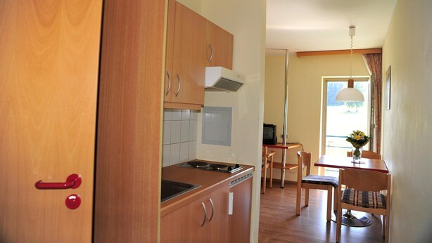 Een functionele keuken met houten kastjes, een fornuis en een eethoek met een tafel en stoelen.