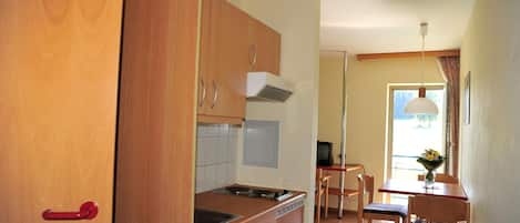 Una cocina compacta con armarios de madera, un fogón y un comedor con mesa y sillas.