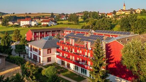 Een meerlaags gebouw met zonnepanelen op het dak, omgeven door groen en andere gebouwen.