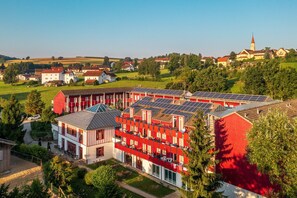 A multi-story building with solar panels on the roof, surrounded by greenery and other buildings. - Appartement mit All inklusive Angebot und Pool (Runding)