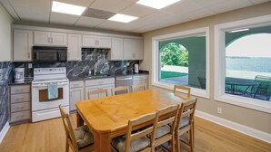 Una cocina con armarios blancos, un microondas negro y una mesa de comedor de madera con sillas.