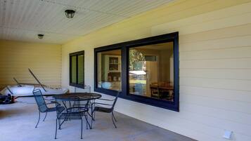 A covered patio area with a table and chairs, large windows, and a ceiling light fixture.