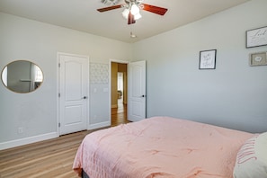 Ein Schlafzimmer mit einem Bett, einem Deckenventilator, einer Tür und einem Flur, der in ein weiteres Zimmer führt.
