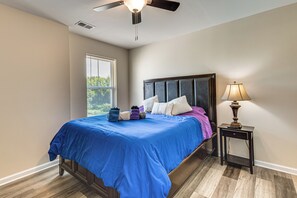 Un dormitorio con cama, mesita de noche, lámpara, ventilador de techo y ventana con persianas.