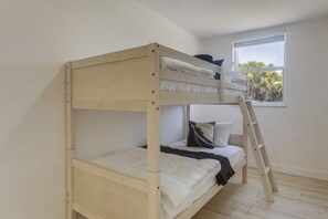 Ein Stockbett mit einer Leiter, weißer Bettwäsche und einem Fenster mit Blick auf Grünflächen.