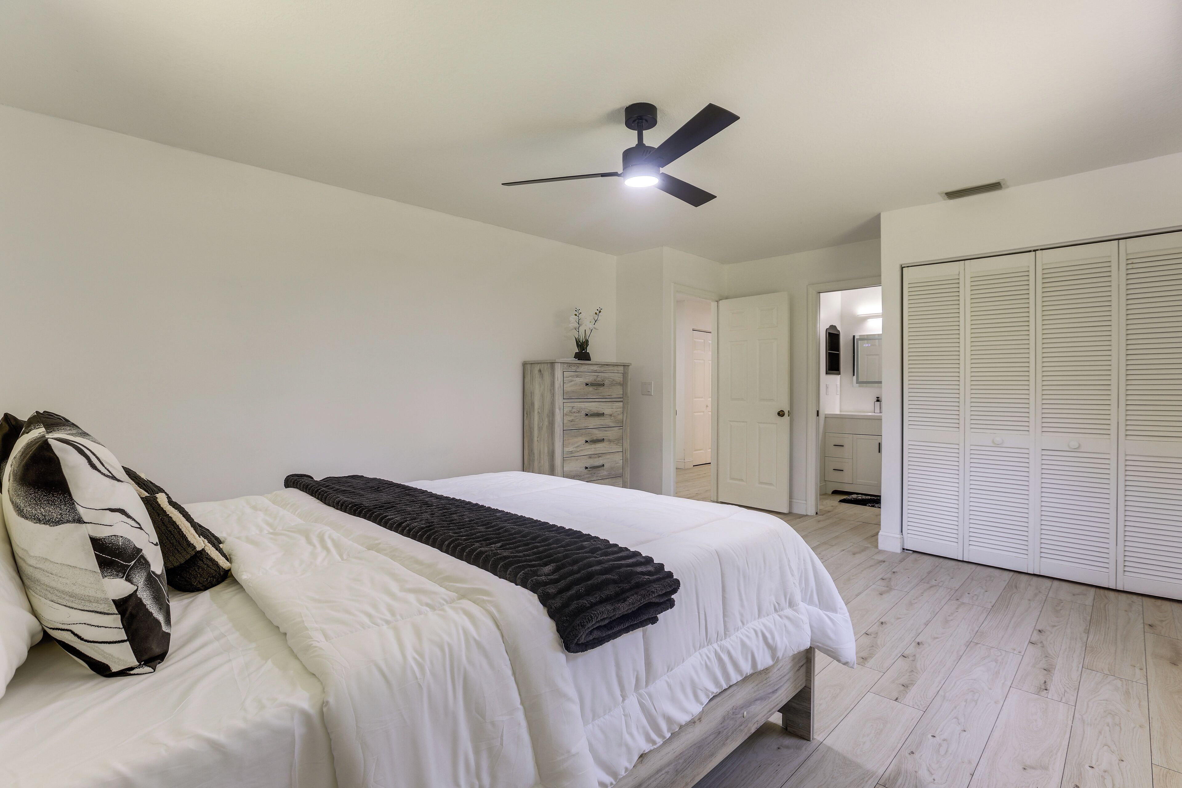 A bedroom with a bed, a ceiling fan, a dresser, and a walk-in closet.