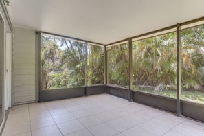 Ein Zimmer mit großen Fenstern, Fliesenboden und Blick auf üppiges Grün.