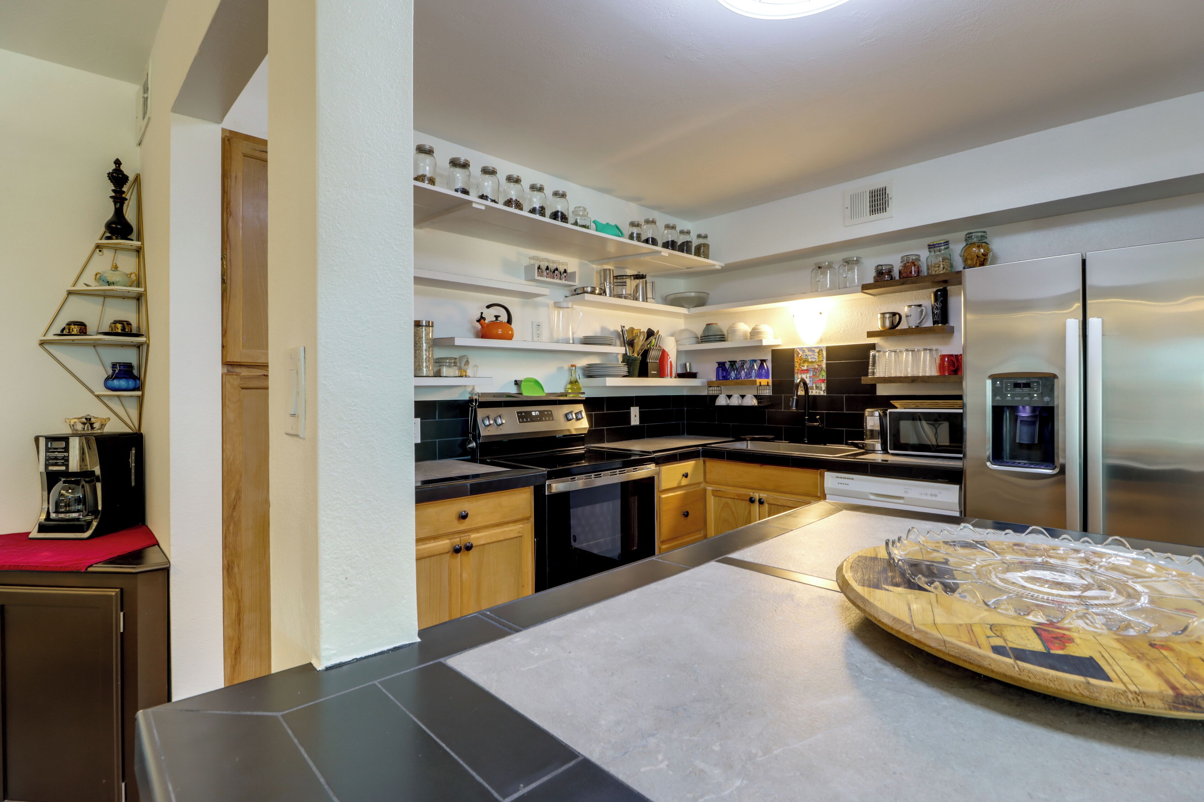 Een moderne keuken met een zwart aanrecht, roestvrijstalen apparatuur en diverse opbergpotten op de planken.