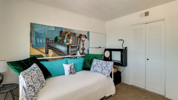 Ein Schlafzimmer mit einem Bett, einem Bild an der Wand, einem Schreibtisch mit Computer und einem Kleiderschrank.