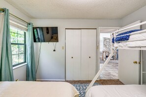 Ein Zimmer mit Etagenbetten, einer Tür, einem Fenster mit Vorhängen und einem an der Wand befestigten Fernseher.