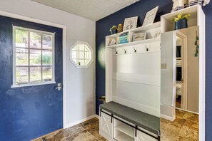 Ein Zimmer mit blauer Tür, Fenster, weißer Wand, einem Regal mit Haken und einer Bank.