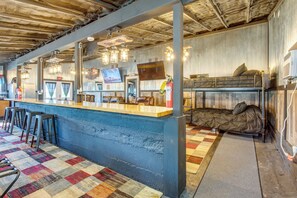 A bar area with stools, a counter, and a television screen. There is a bunk bed with pillows and a fire extinguisher. - Cast & Relax! Lake-View Fishing Cabin in Monmouth (Monmouth)