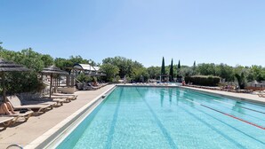 Una piscina cristalina con sillas de descanso y sombrillas, rodeada de árboles y un pabellón.
