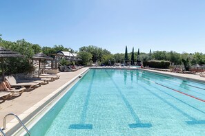 A clear swimming pool with lounge chairs and umbrellas, surrounded by trees and a gazebo.