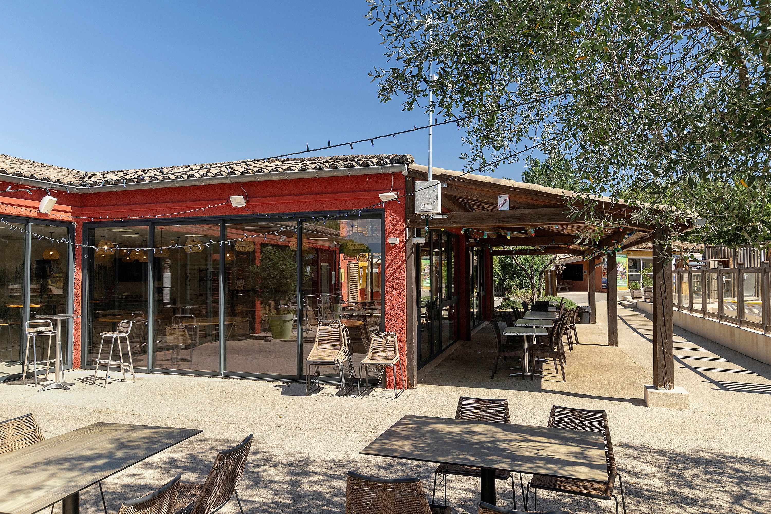 An outdoor cafe with tables and chairs, a red-roofed structure, and a clear sky.