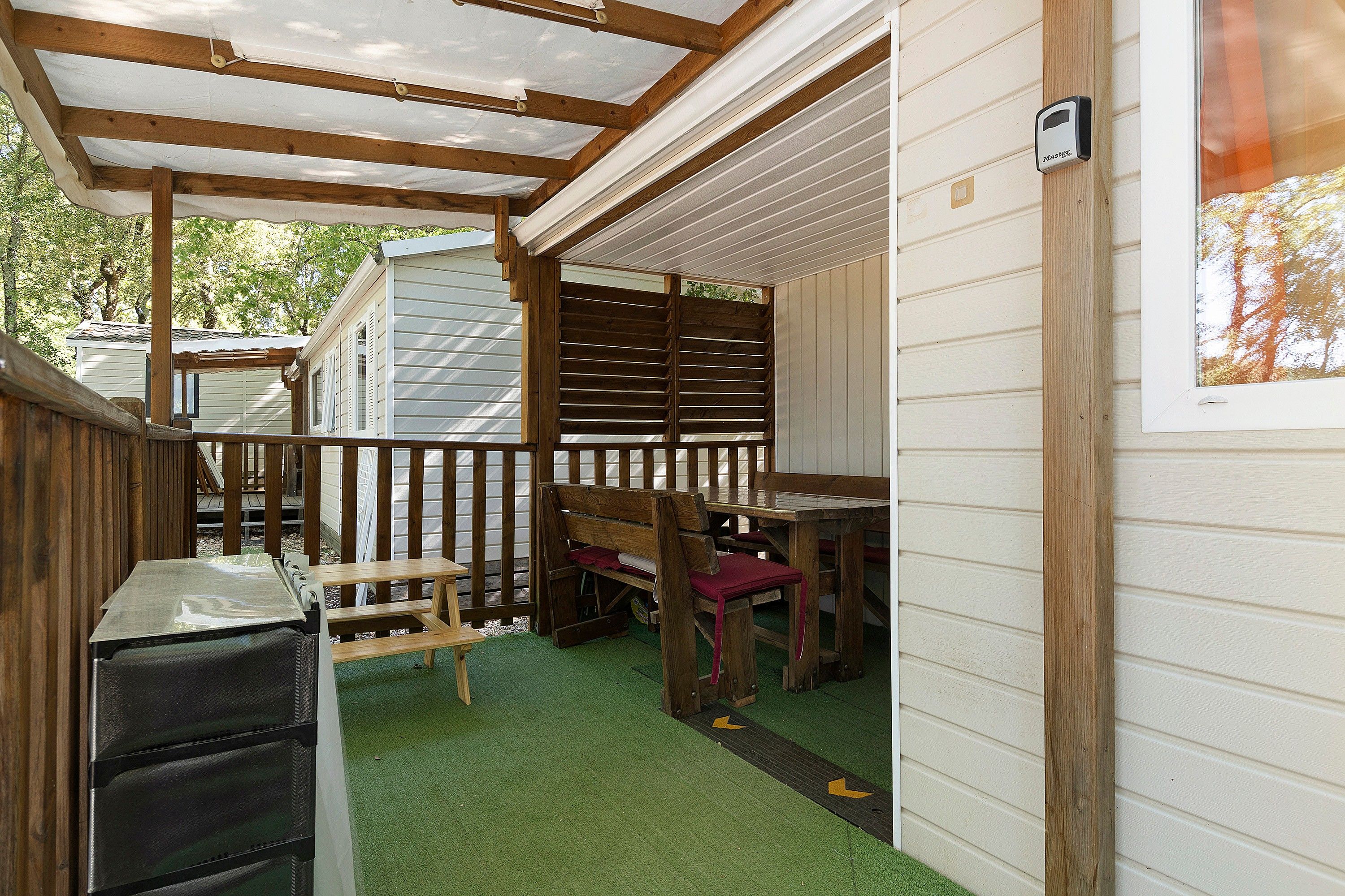 A covered outdoor area with a wooden bench, a table, and a green artificial turf floor.