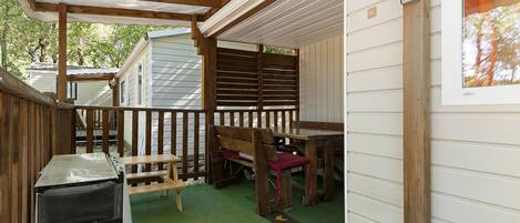 A covered outdoor area with a wooden bench, a table, and a green artificial turf floor.