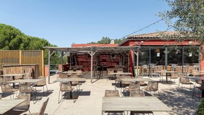 Un área de patio al aire libre con mesas y sillas, una valla de madera y un edificio con techo rojo al fondo.