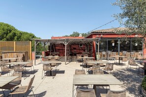 An outdoor seating area with tables and chairs, a wooden fence, and a building with a red roof in the background.