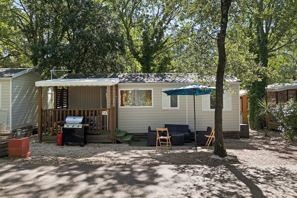 A single-story mobile home with a patio area, a grill, and outdoor seating.