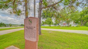 A historical marker sign in a grassy area with a road and a house in the background. - Recently Remodeled Route 66 Retreat! Claremore Gem (Claremore)