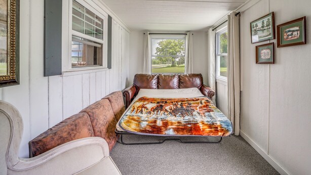 A narrow hallway with a bed at the end, a window with curtains, and framed pictures on the wall. - Recently Remodeled Route 66 Retreat! Claremore Gem (Claremore)