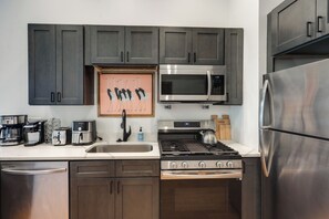 A modern kitchen with stainless steel appliances, dark wooden cabinets, and a framed artwork above the sink. - Walkable & Stylish! Cincy Loft in Prime OTR Spot (Cincinnati)