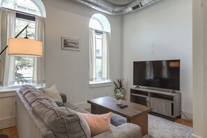Un saló modern amb un sofà modular, un televisor de pantalla plana i un gran finestral amb vista a arbres.
