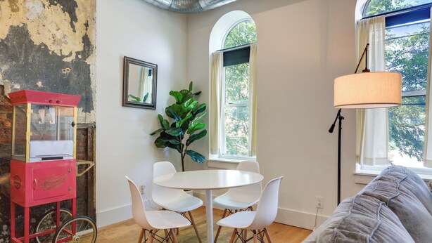 Une pièce avec une table et des chaises blanches, un distributeur de pop-corn rouge de style rétro, une grande plante verte et une fenêtre donnant sur des arbres.