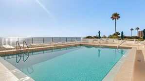 En klarblå pool med en skylt som anger ett maximalt djup på 1,8 meter, omgiven av solstolar och en palm.