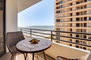 A balcony with a view of the ocean, a round table, and wicker chairs. - Dream Daytona Getaway: Beachfront Condo! (Daytona Beach)
